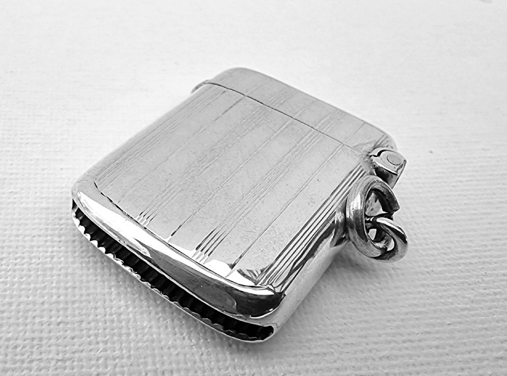 An open antique sterling silver vesta case featuring linear engine-turned engraving, a central circular cartouche, British hallmarks, and a suspension ring. View III
