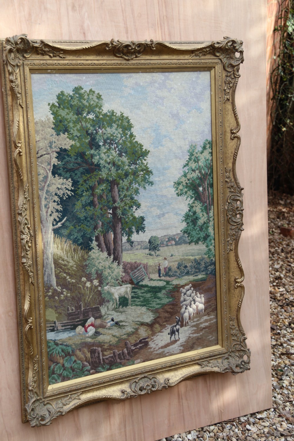A large framed woolwork needlepoint tapestry depicting a pastoral landscape scene enclosed in a heavily ornamented giltwood frame. View IV