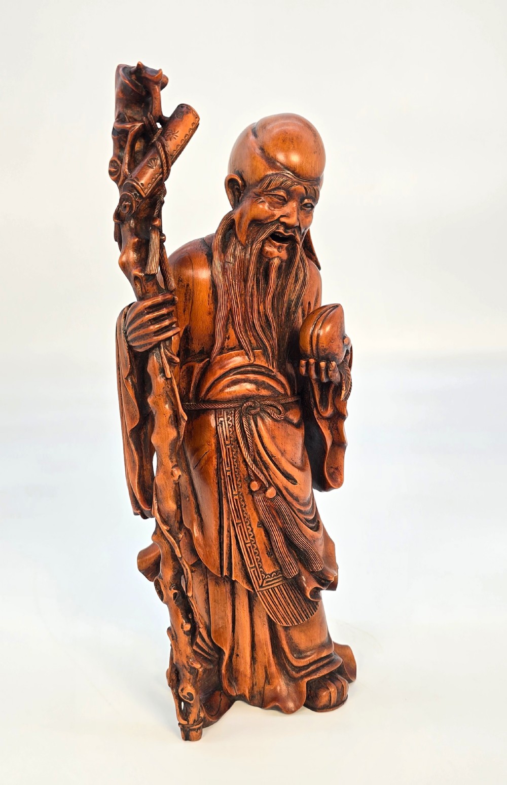 A Japanese carved boxwood okimono figure depicting Fukurokuju with a high forehead, long beard, flowing robes, and holding a gnarled staff.