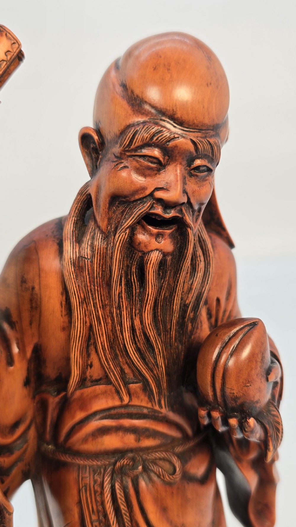A Japanese carved boxwood okimono figure depicting Fukurokuju with a high forehead, long beard, flowing robes, and holding a gnarled staff. View XI