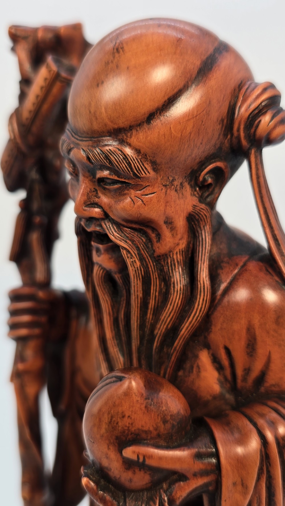 A Japanese carved boxwood okimono figure depicting Fukurokuju with a high forehead, long beard, flowing robes, and holding a gnarled staff. View XII