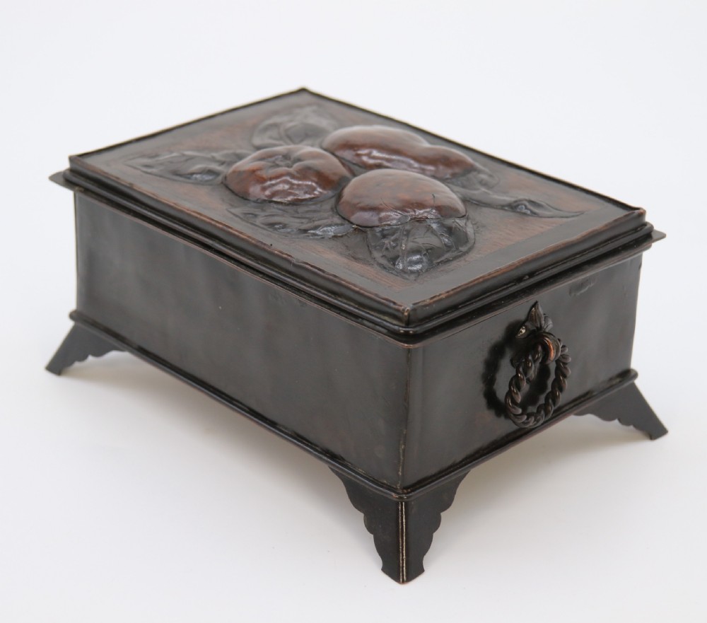 A rectangular dark patinated copper box featuring repousse fruit motifs on the lid, stylized foliage on the front face, bracket feet, and side drop ring handles. View IV