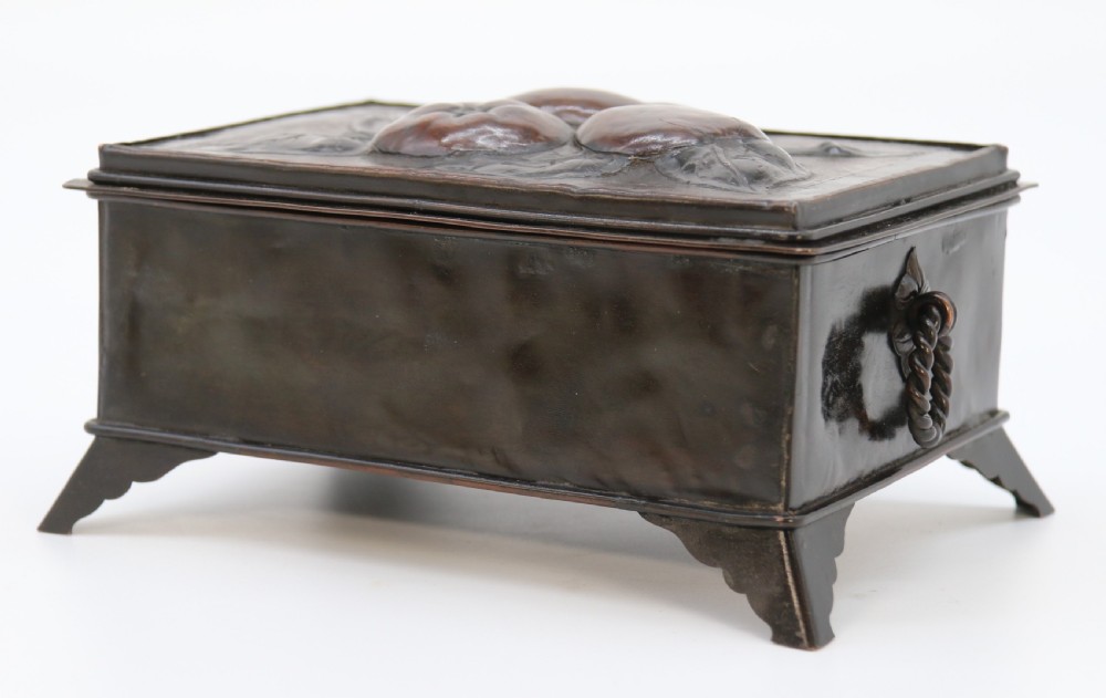 A rectangular dark patinated copper box featuring repousse fruit motifs on the lid, stylized foliage on the front face, bracket feet, and side drop ring handles. View XIV