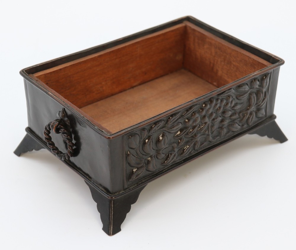 A rectangular dark patinated copper box featuring repousse fruit motifs on the lid, stylized foliage on the front face, bracket feet, and side drop ring handles. View XVI
