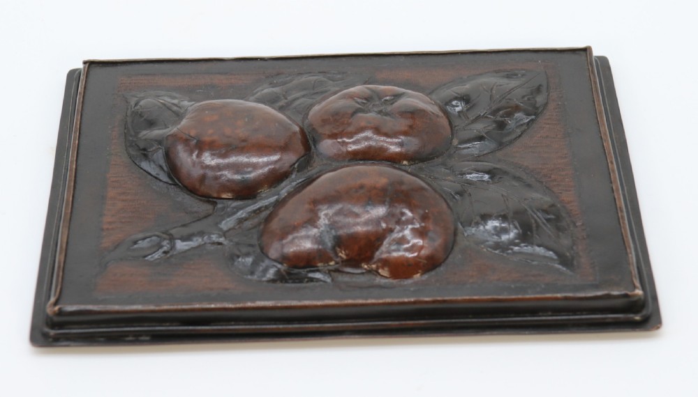 A rectangular dark patinated copper box featuring repousse fruit motifs on the lid, stylized foliage on the front face, bracket feet, and side drop ring handles. View XX