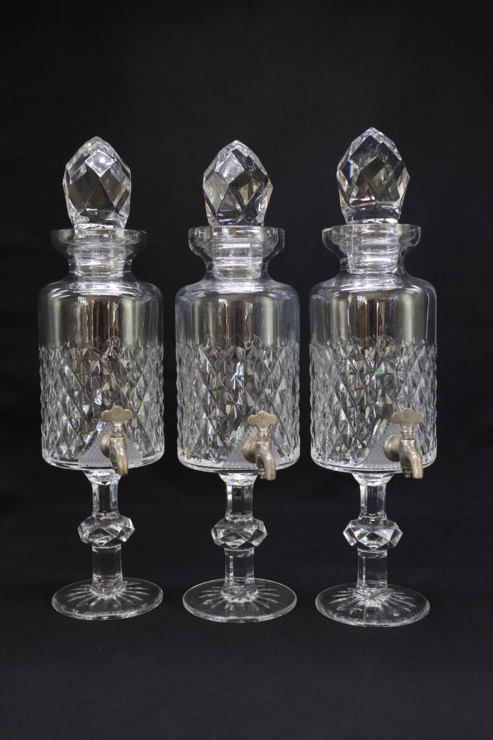 A set of five cut crystal perfume display bottles with faceted stoppers, diamond cut bodies, and silver spigots. View XII