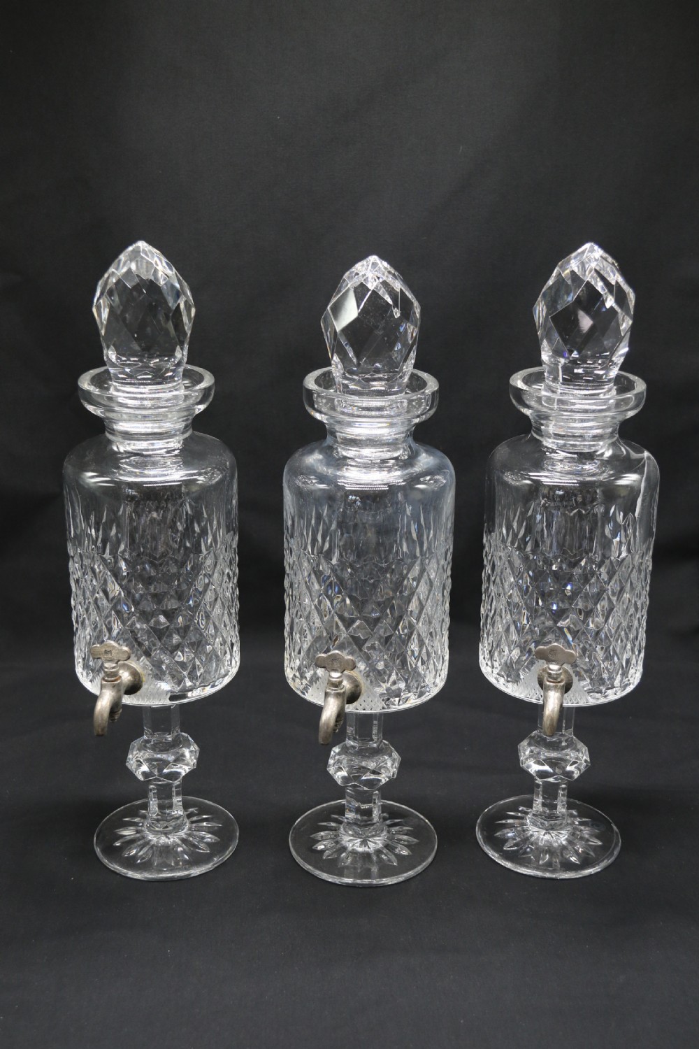 A set of five cut crystal perfume display bottles with faceted stoppers, diamond cut bodies, and silver spigots. View XVII