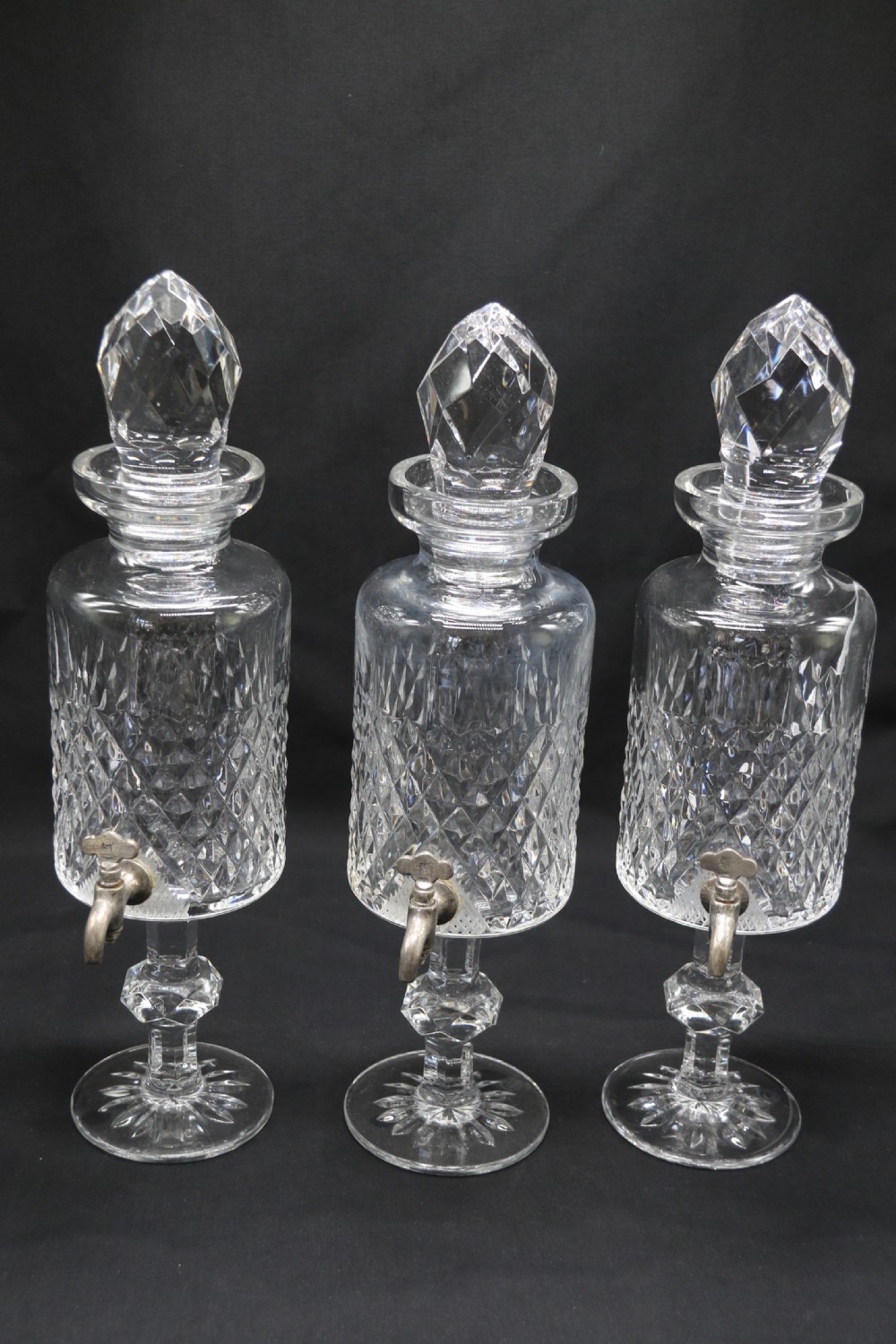 A set of five cut crystal perfume display bottles with faceted stoppers, diamond cut bodies, and silver spigots. View XVIII