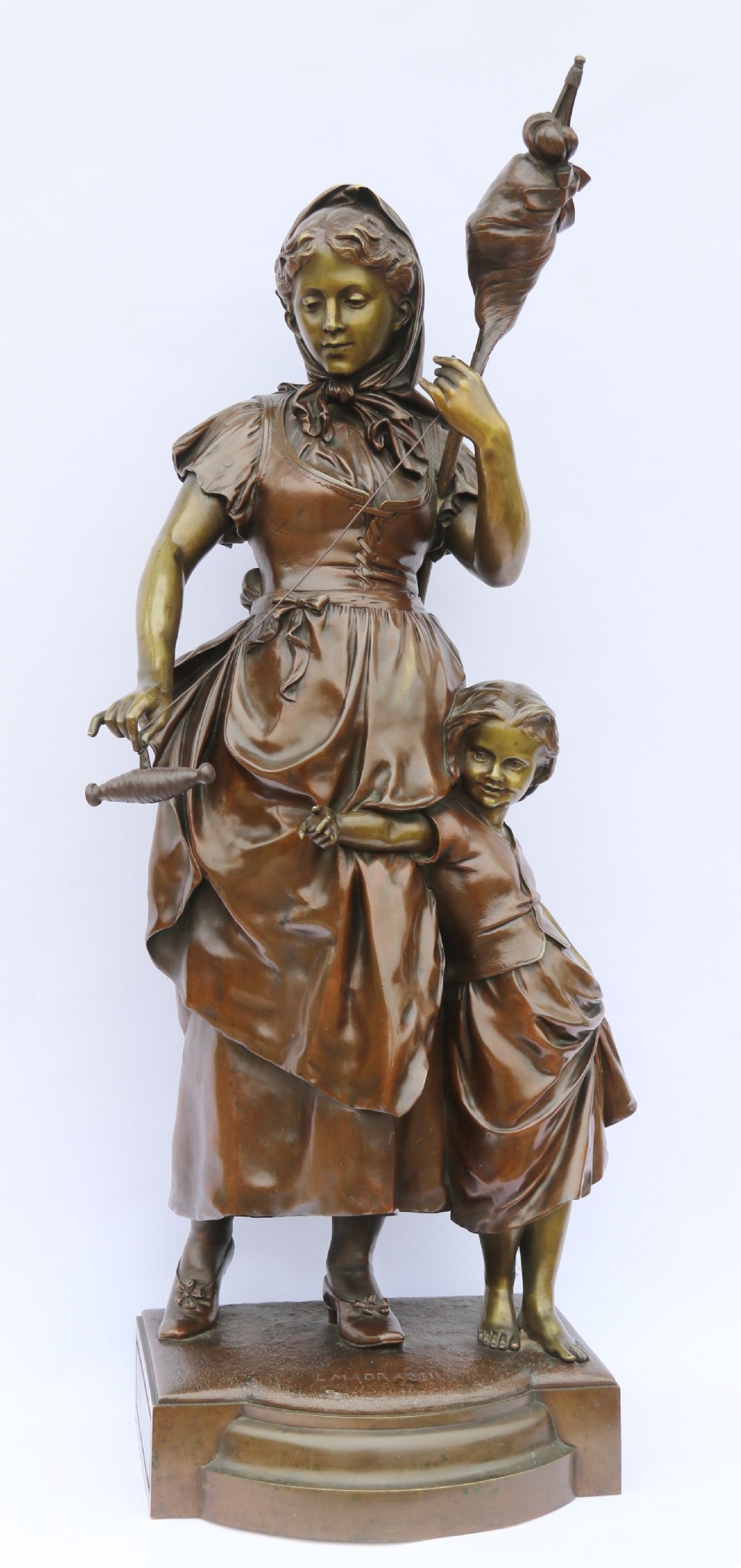 A late nineteenth-century patinated bronze sculpture depicting a woman holding a spinning distaff beside a young child clinging to her skirt.