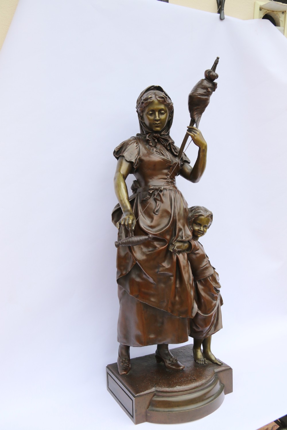 A late nineteenth-century patinated bronze sculpture depicting a woman holding a spinning distaff beside a young child clinging to her skirt. View XV