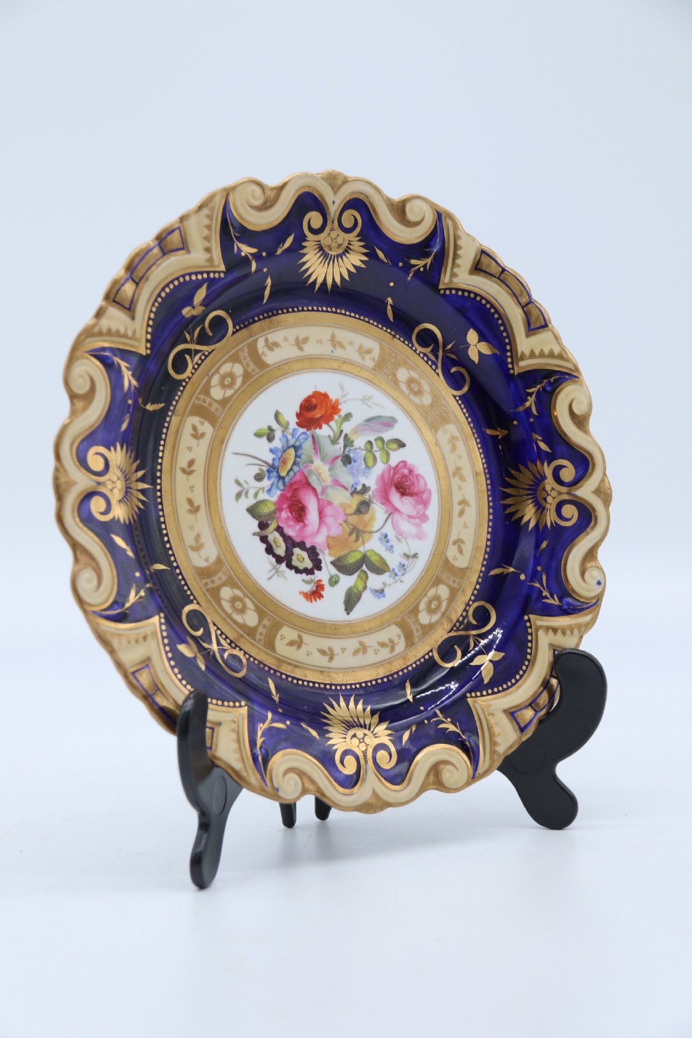 An antique circular English porcelain cabinet plate featuring a cobalt blue and gold scroll border surrounding a central hand-painted floral bouquet.