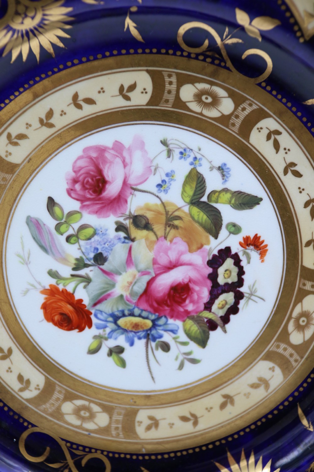 An antique circular English porcelain cabinet plate featuring a cobalt blue and gold scroll border surrounding a central hand-painted floral bouquet. View III
