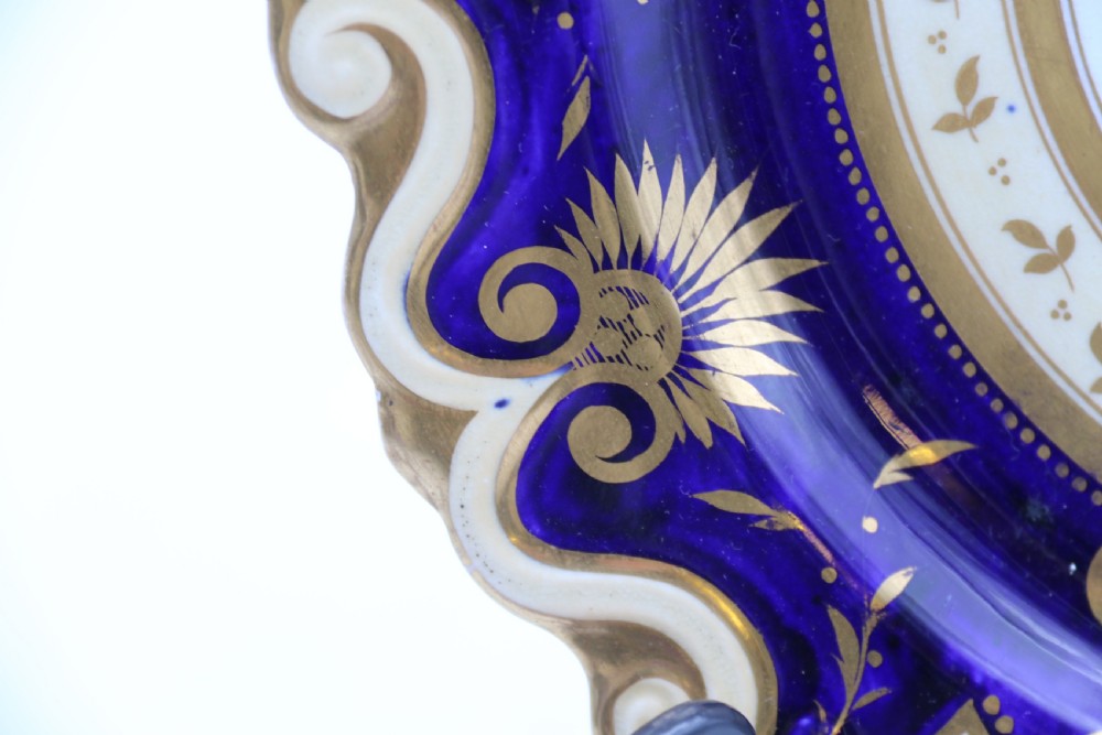 An antique circular English porcelain cabinet plate featuring a cobalt blue and gold scroll border surrounding a central hand-painted floral bouquet. View V