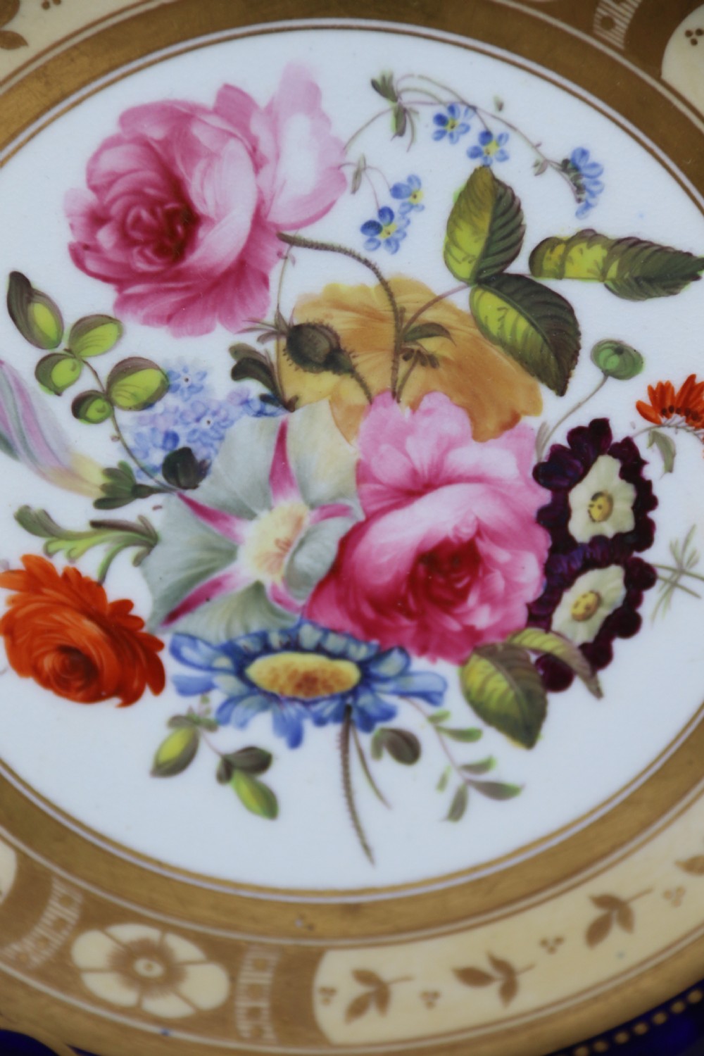 An antique circular English porcelain cabinet plate featuring a cobalt blue and gold scroll border surrounding a central hand-painted floral bouquet. View VII