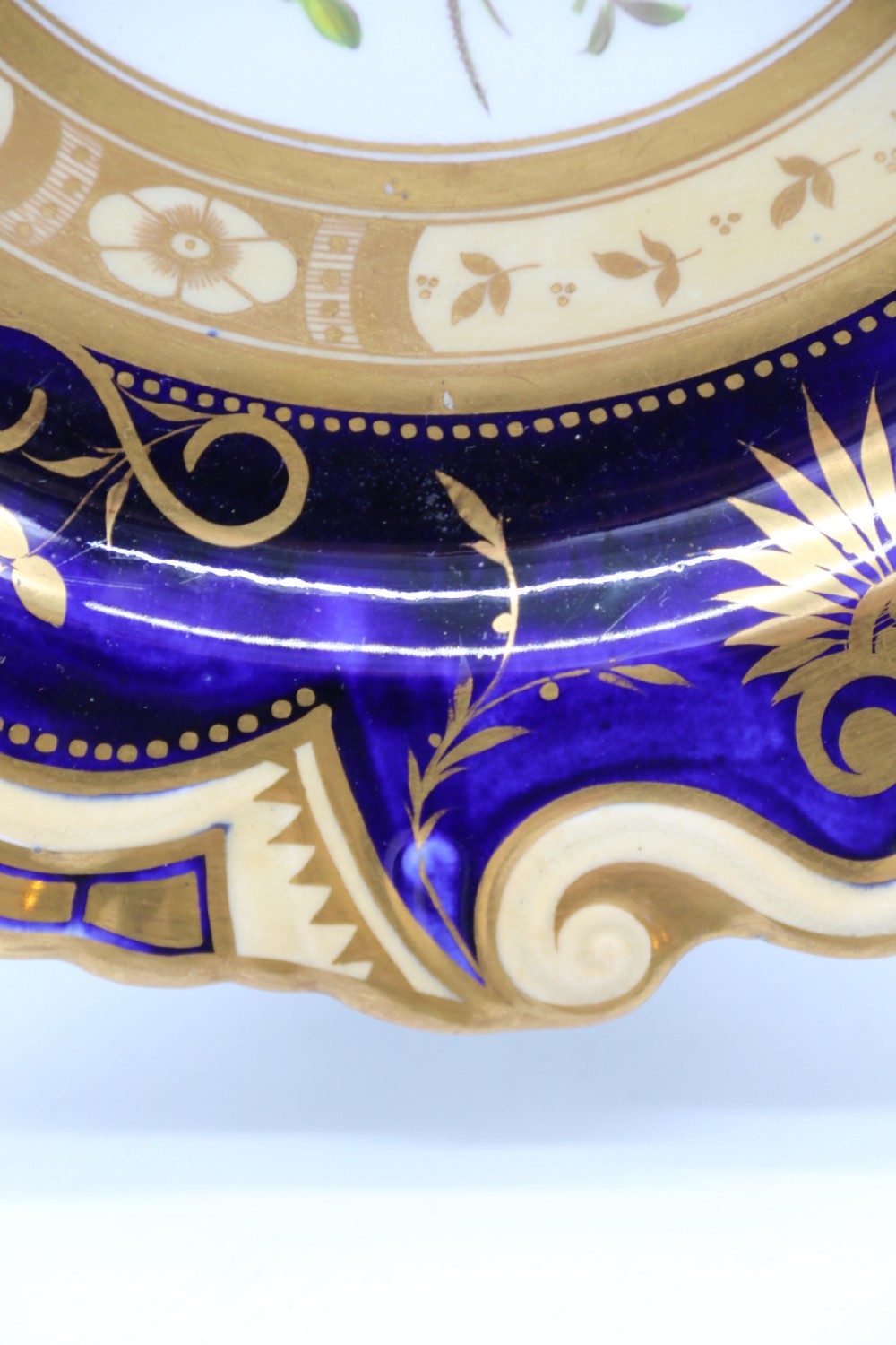 An antique circular English porcelain cabinet plate featuring a cobalt blue and gold scroll border surrounding a central hand-painted floral bouquet. View VIII
