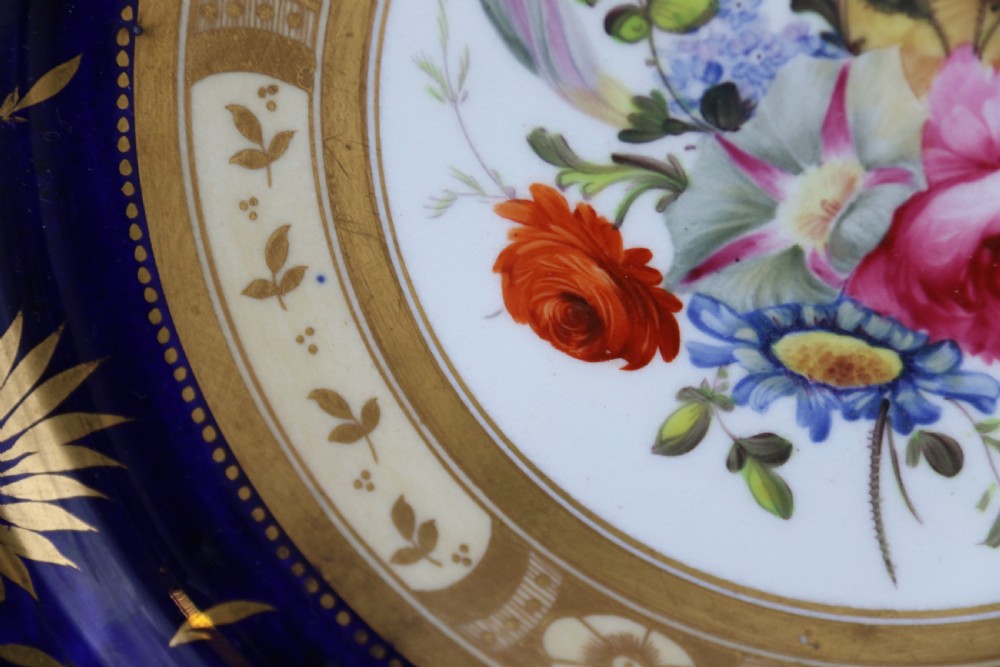 An antique circular English porcelain cabinet plate featuring a cobalt blue and gold scroll border surrounding a central hand-painted floral bouquet. View X