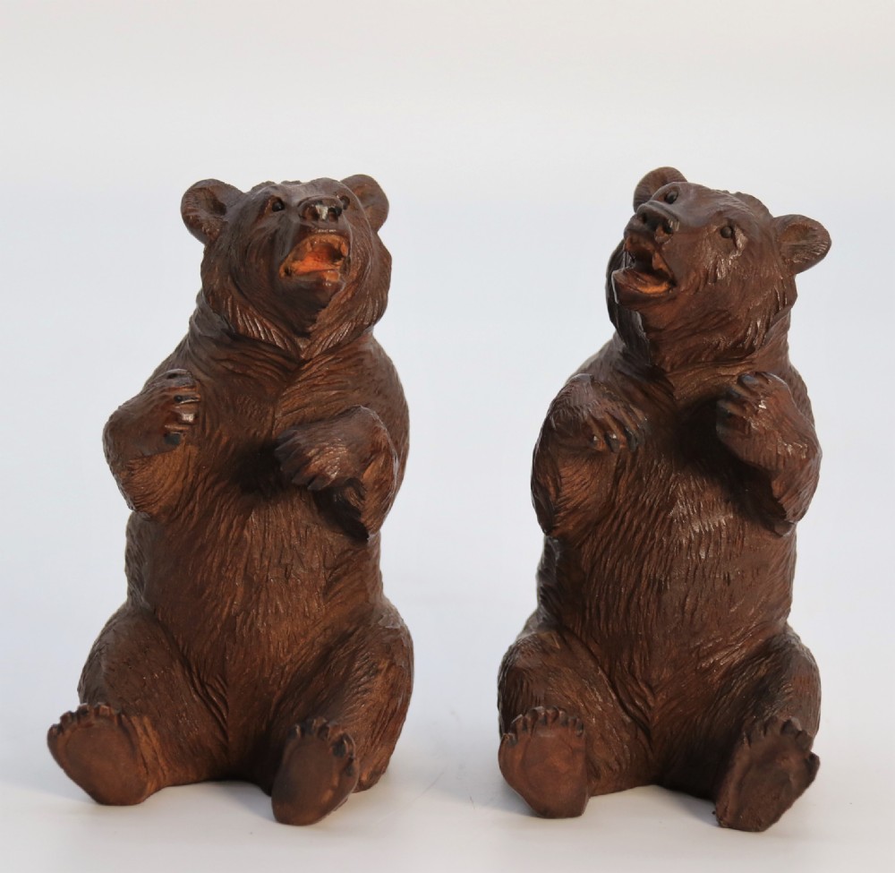 A pair of hand-carved dark brown linden wood Black Forest bears depicted sitting on their haunches with open jaws.
