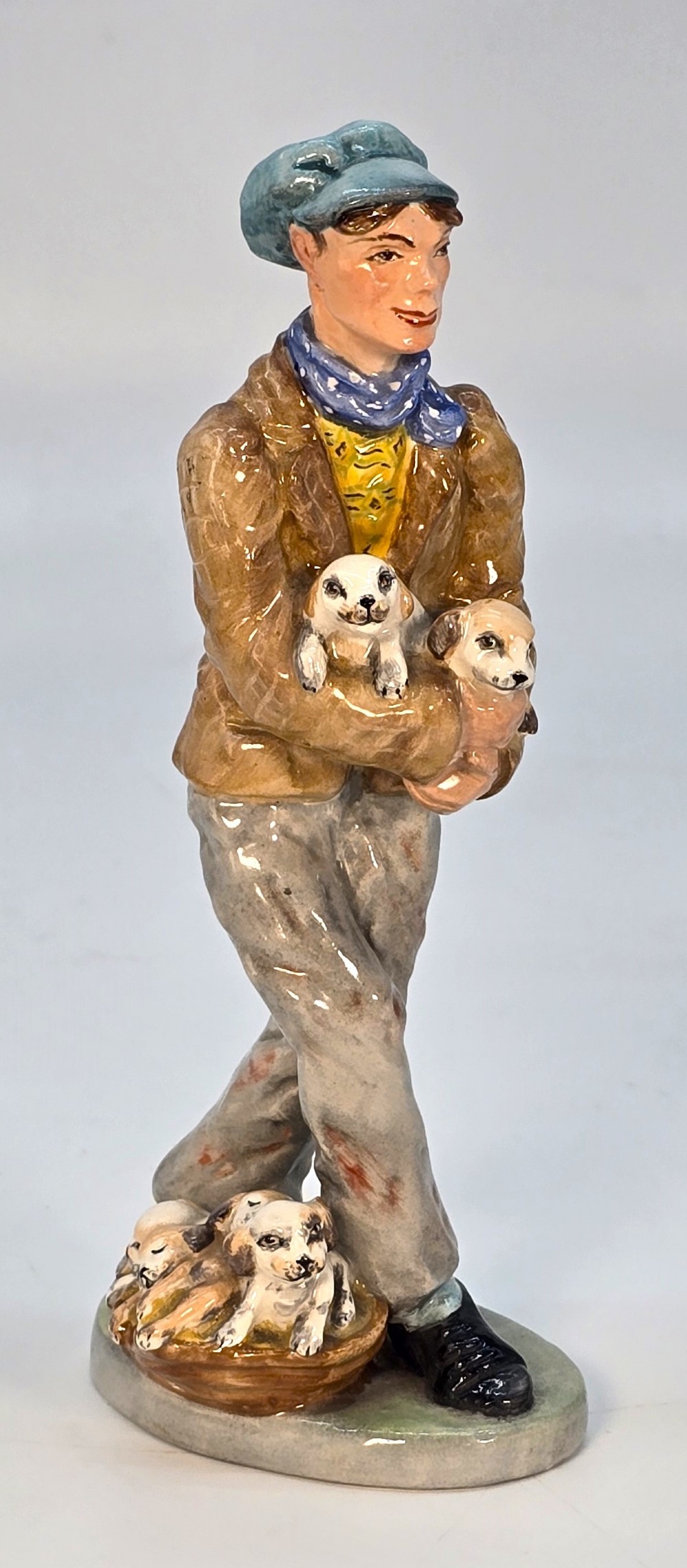 A hand-painted Edwardian ceramic statuette depicting a man holding puppies with a basket of dogs at his feet.