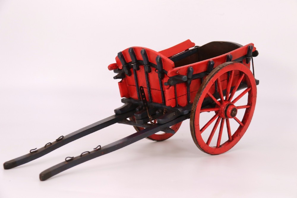 A detailed handmade wooden scale model of an 18th-century farm cart featuring red painted sides, dark blue framing and shafts, and spoked red wheels.