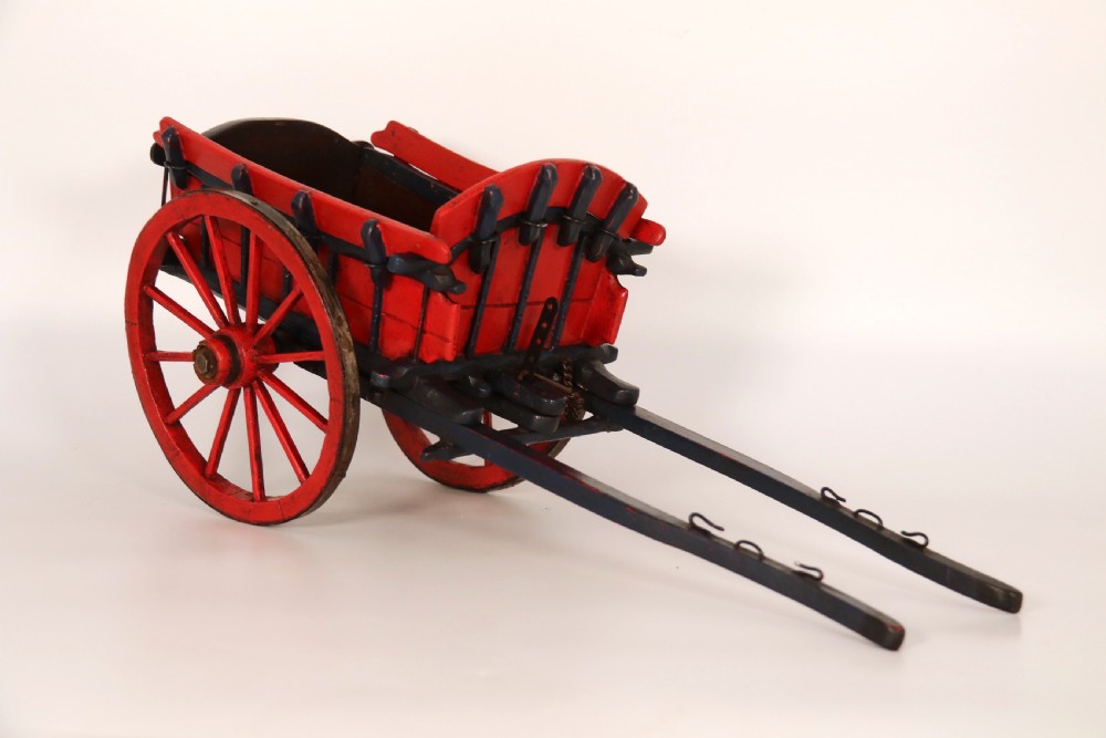 A detailed handmade wooden scale model of an 18th-century farm cart featuring red painted sides, dark blue framing and shafts, and spoked red wheels. View II