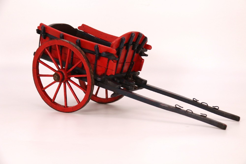 A detailed handmade wooden scale model of an 18th-century farm cart featuring red painted sides, dark blue framing and shafts, and spoked red wheels. View V
