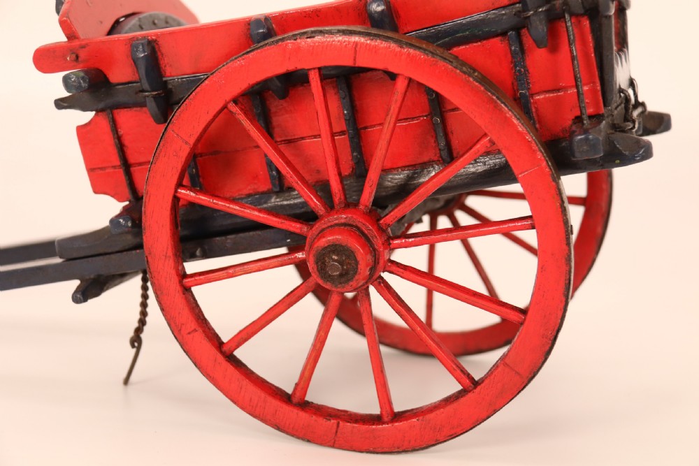 A detailed handmade wooden scale model of an 18th-century farm cart featuring red painted sides, dark blue framing and shafts, and spoked red wheels. View XIII