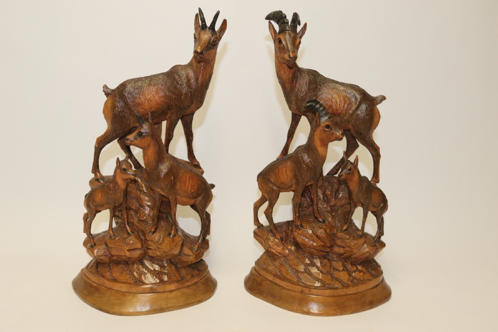 A pair of hand-carved wooden sculptures depicting ibex and chamois with offspring on carved rocky bases. View XXX