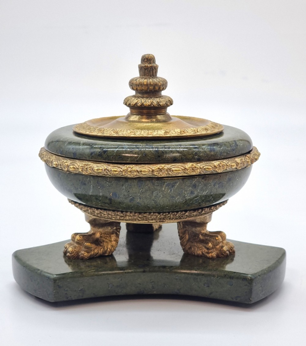 A French Empire style green marble inkstand featuring a central urn-shaped vessel with gilt bronze floral borders and a decorative finial lid, supported by three lion paw feet on a curved marble base. View II