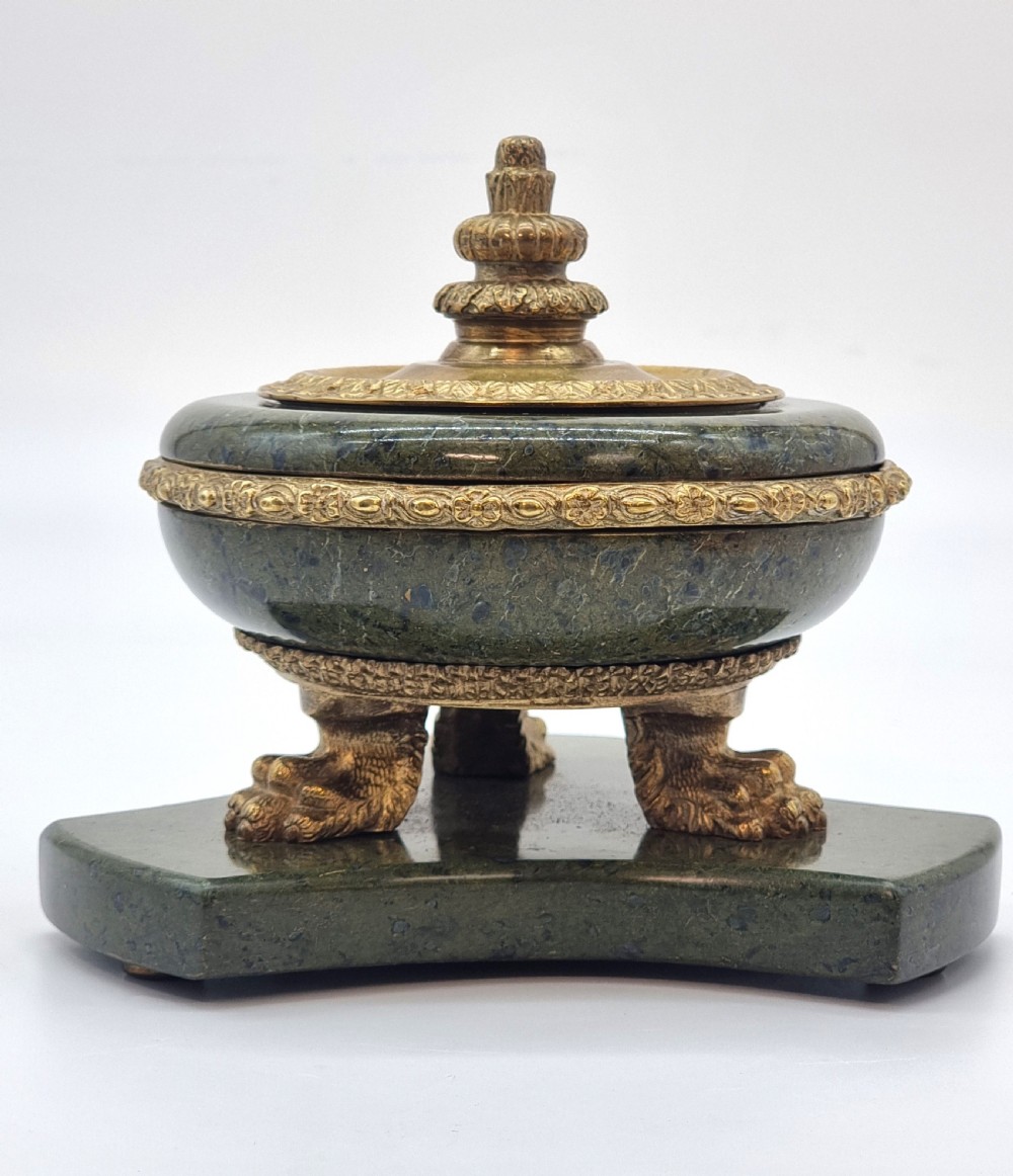 A French Empire style green marble inkstand featuring a central urn-shaped vessel with gilt bronze floral borders and a decorative finial lid, supported by three lion paw feet on a curved marble base. View IV