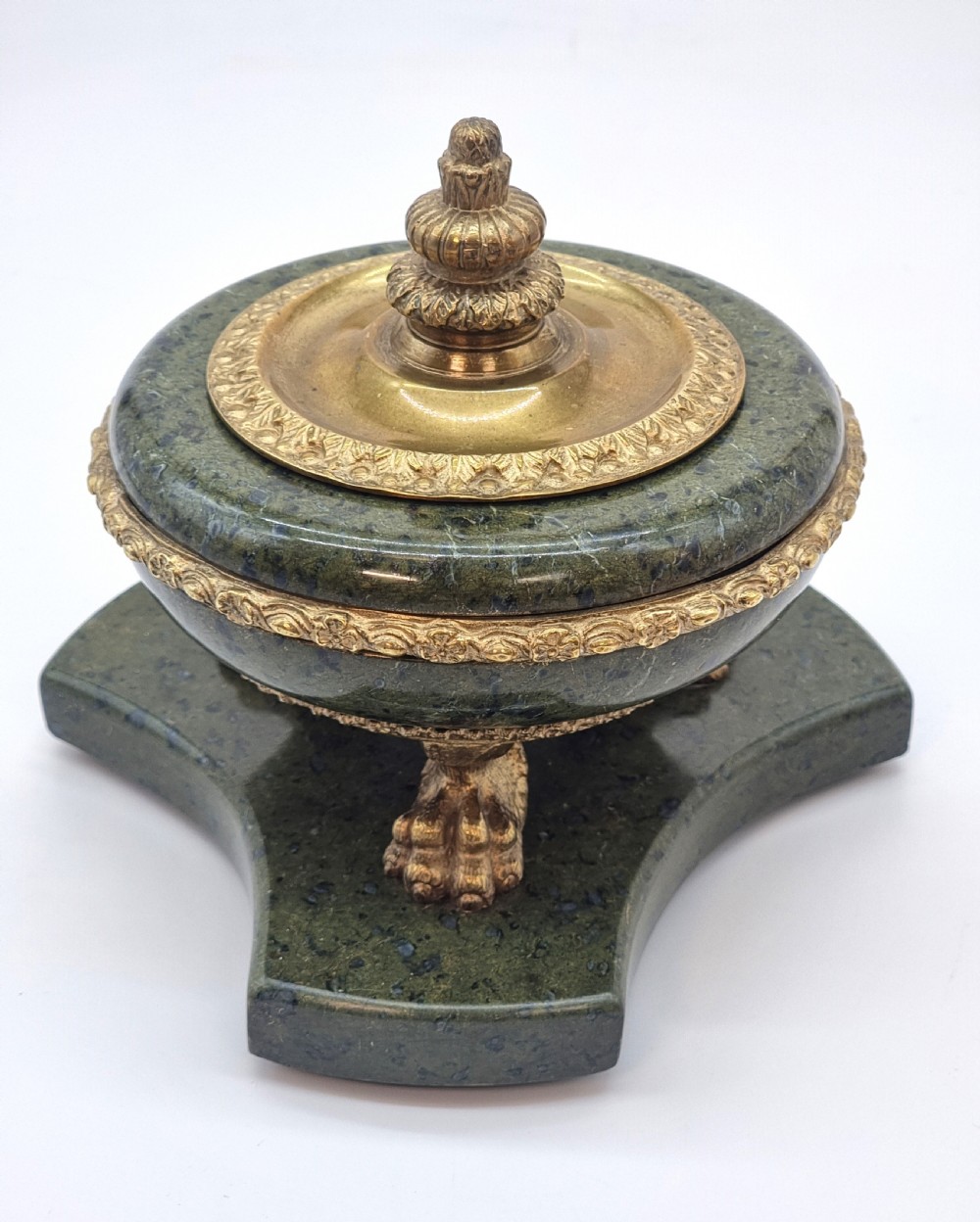 A French Empire style green marble inkstand featuring a central urn-shaped vessel with gilt bronze floral borders and a decorative finial lid, supported by three lion paw feet on a curved marble base. View V