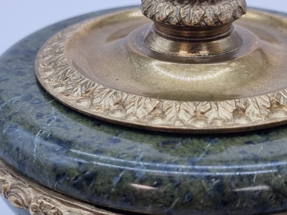 A French Empire style green marble inkstand featuring a central urn-shaped vessel with gilt bronze floral borders and a decorative finial lid, supported by three lion paw feet on a curved marble base. View VII