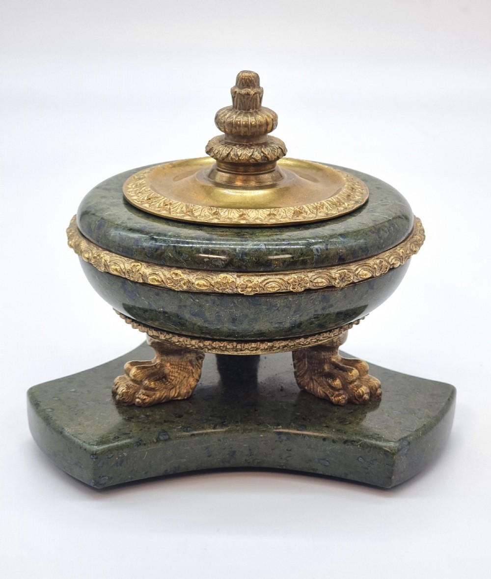 A French Empire style green marble inkstand featuring a central urn-shaped vessel with gilt bronze floral borders and a decorative finial lid, supported by three lion paw feet on a curved marble base. View IX