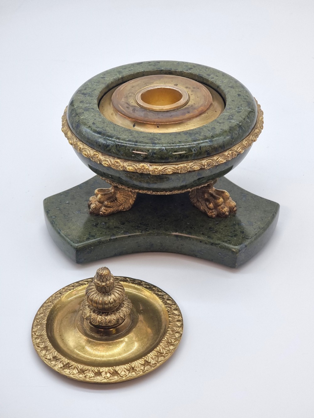 A French Empire style green marble inkstand featuring a central urn-shaped vessel with gilt bronze floral borders and a decorative finial lid, supported by three lion paw feet on a curved marble base. View X