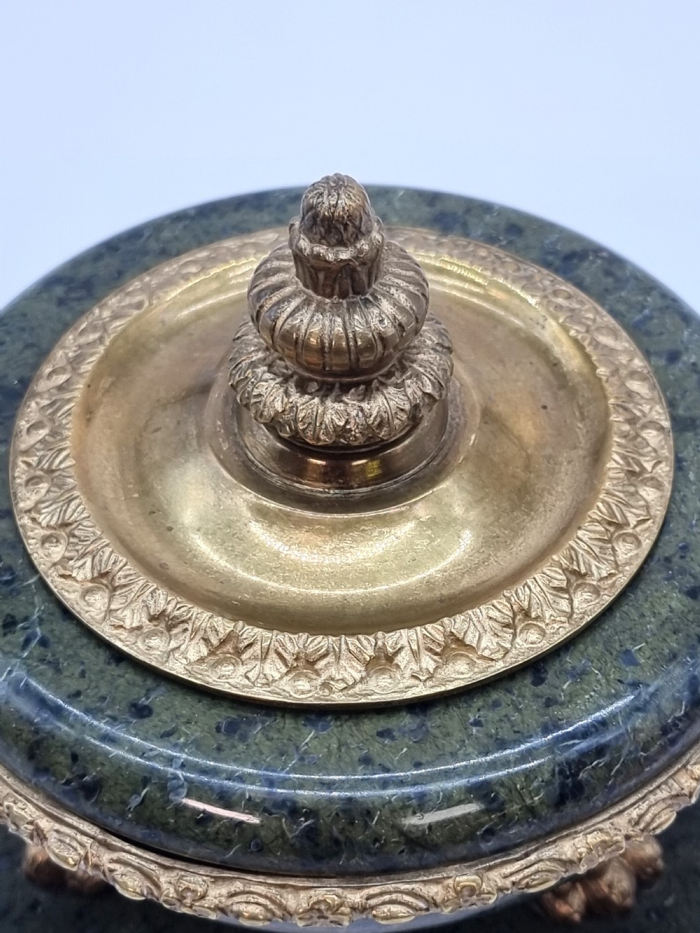 A French Empire style green marble inkstand featuring a central urn-shaped vessel with gilt bronze floral borders and a decorative finial lid, supported by three lion paw feet on a curved marble base. View XV