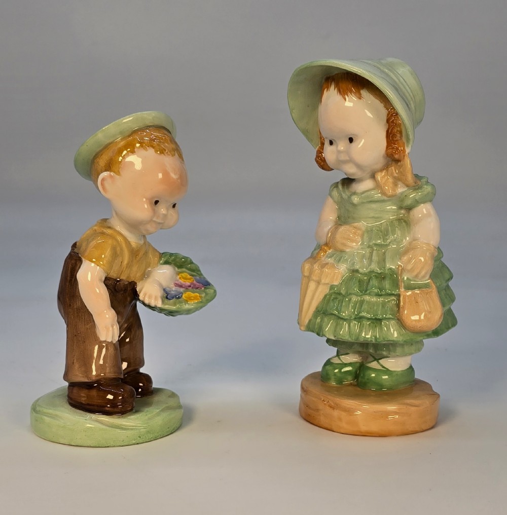 A pair of 1930s Shelley porcelain figures designed by Mabel Lucie Attwell, depicting a boy in brown dungarees with a flower basket alongside a girl in a green bonnet and ruffled dress.