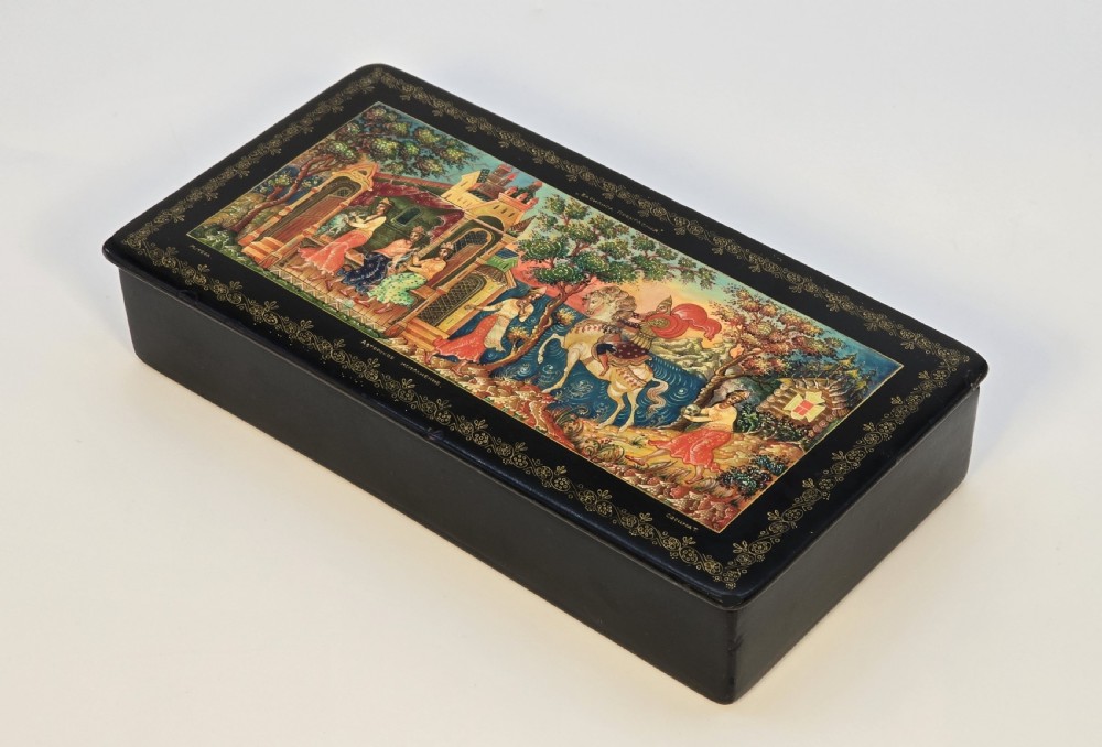 A rectangular black lacquered papier-mache box featuring a detailed hand-painted scene from Russian folklore framed by a delicate gold filigree border. View III