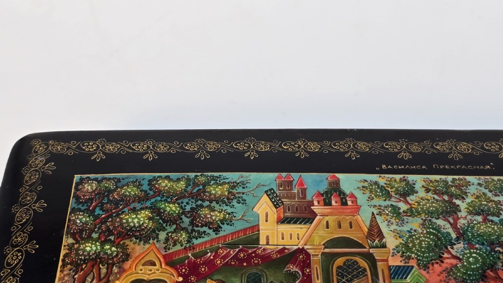 A rectangular black lacquered papier-mache box featuring a detailed hand-painted scene from Russian folklore framed by a delicate gold filigree border. View XI