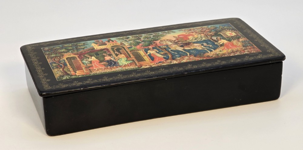 A rectangular black lacquered papier-mache box featuring a detailed hand-painted scene from Russian folklore framed by a delicate gold filigree border. View XIII