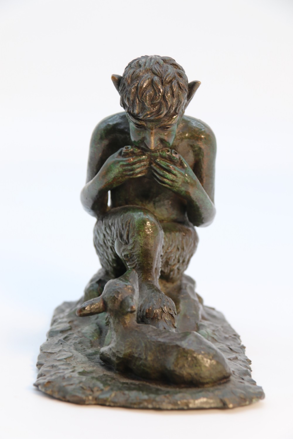 A dark brown patinated bronze sculpture depicting the mythological figure Pan crouching while playing panpipes to a small fawn sitting before him. View III