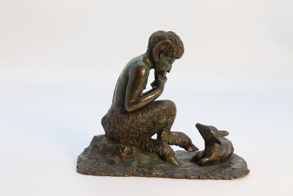 A dark brown patinated bronze sculpture depicting the mythological figure Pan crouching while playing panpipes to a small fawn sitting before him. View VI