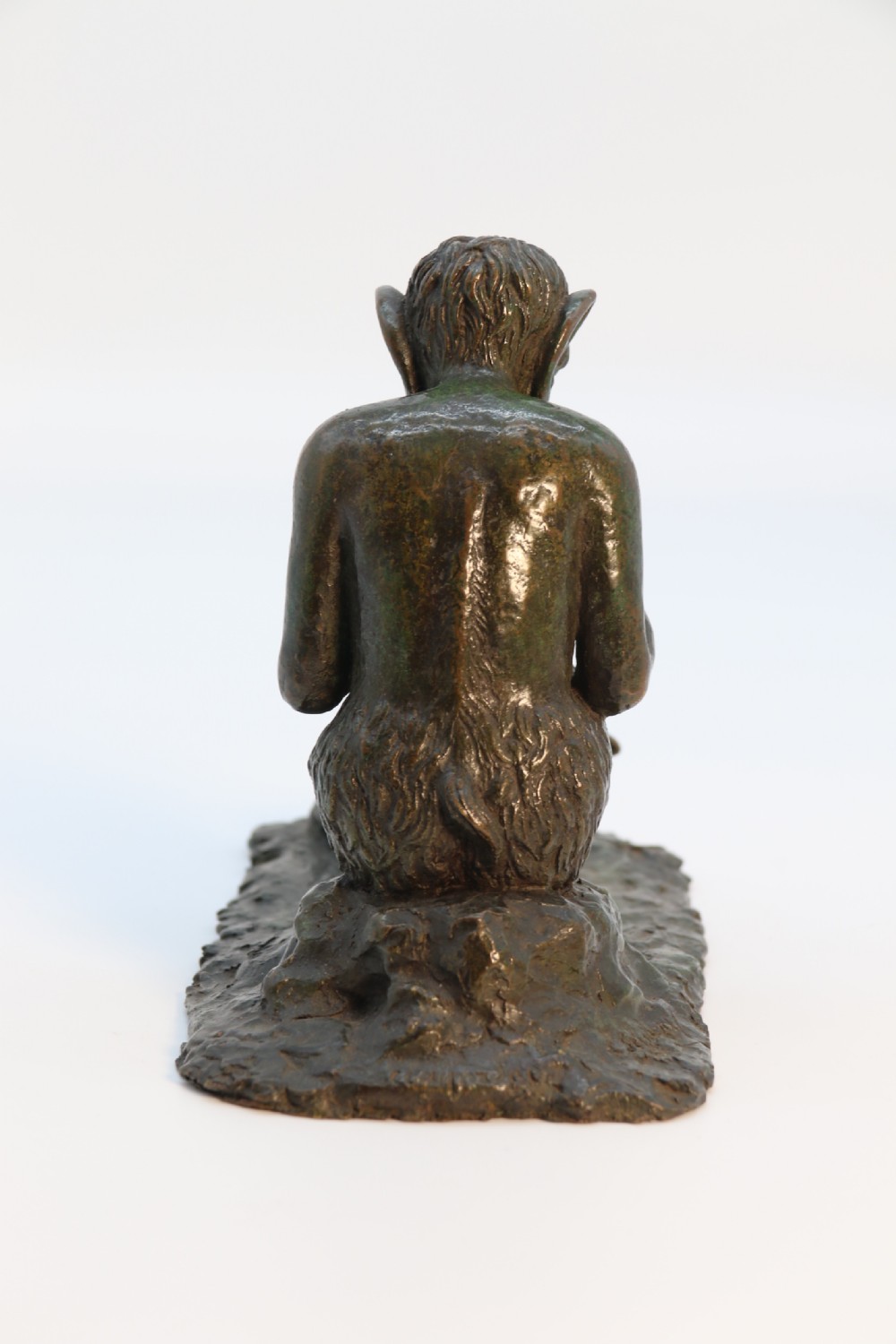 A dark brown patinated bronze sculpture depicting the mythological figure Pan crouching while playing panpipes to a small fawn sitting before him. View VIII