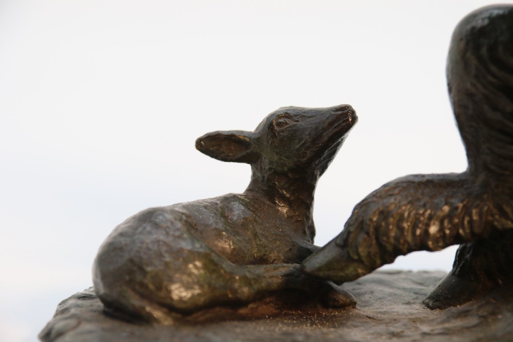 A dark brown patinated bronze sculpture depicting the mythological figure Pan crouching while playing panpipes to a small fawn sitting before him. View X