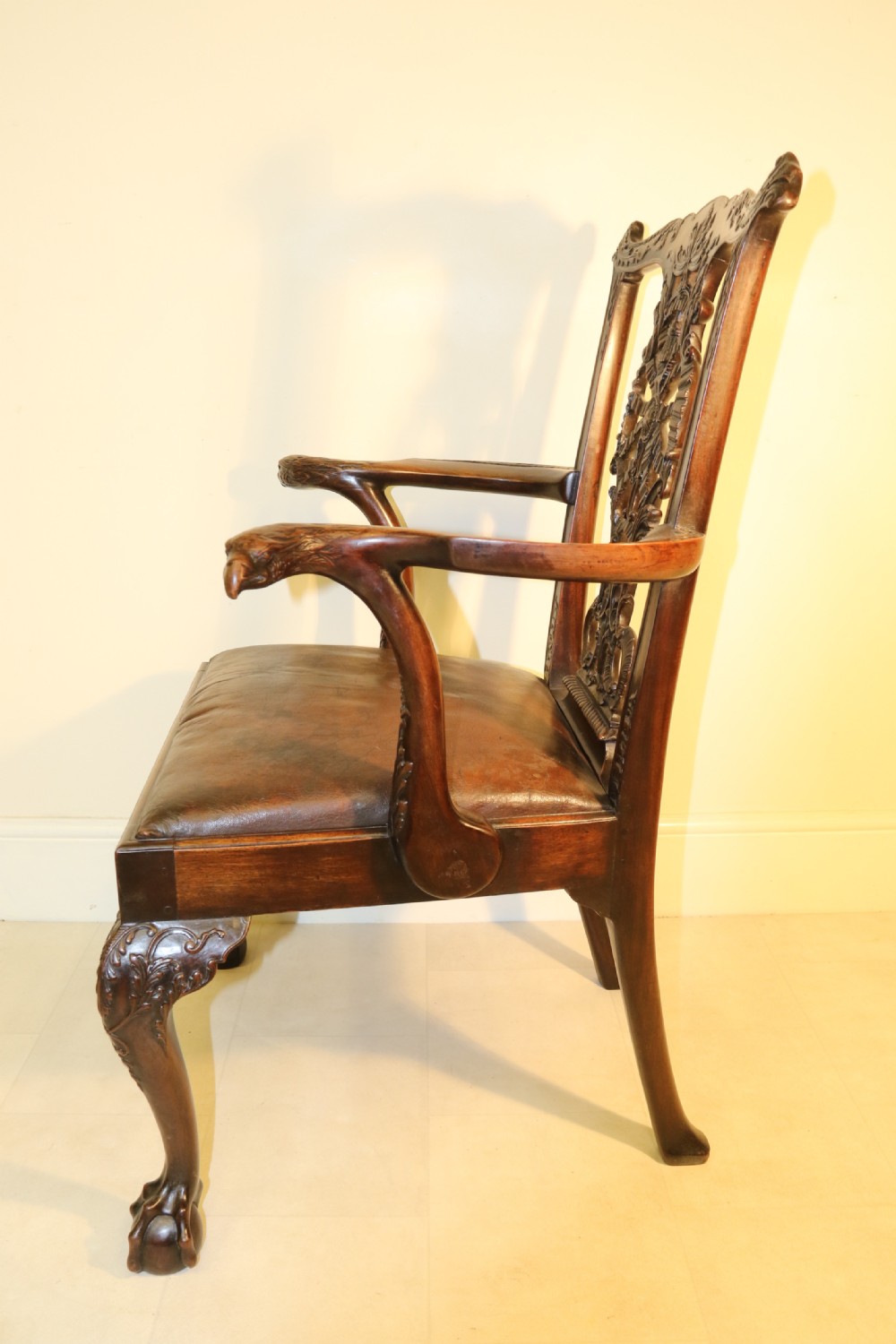 A late 19th-century Chippendale style mahogany armchair featuring carved eagle head terminals, a pierced back splat, brown leather seat, and cabriole legs with claw and ball feet. View XV