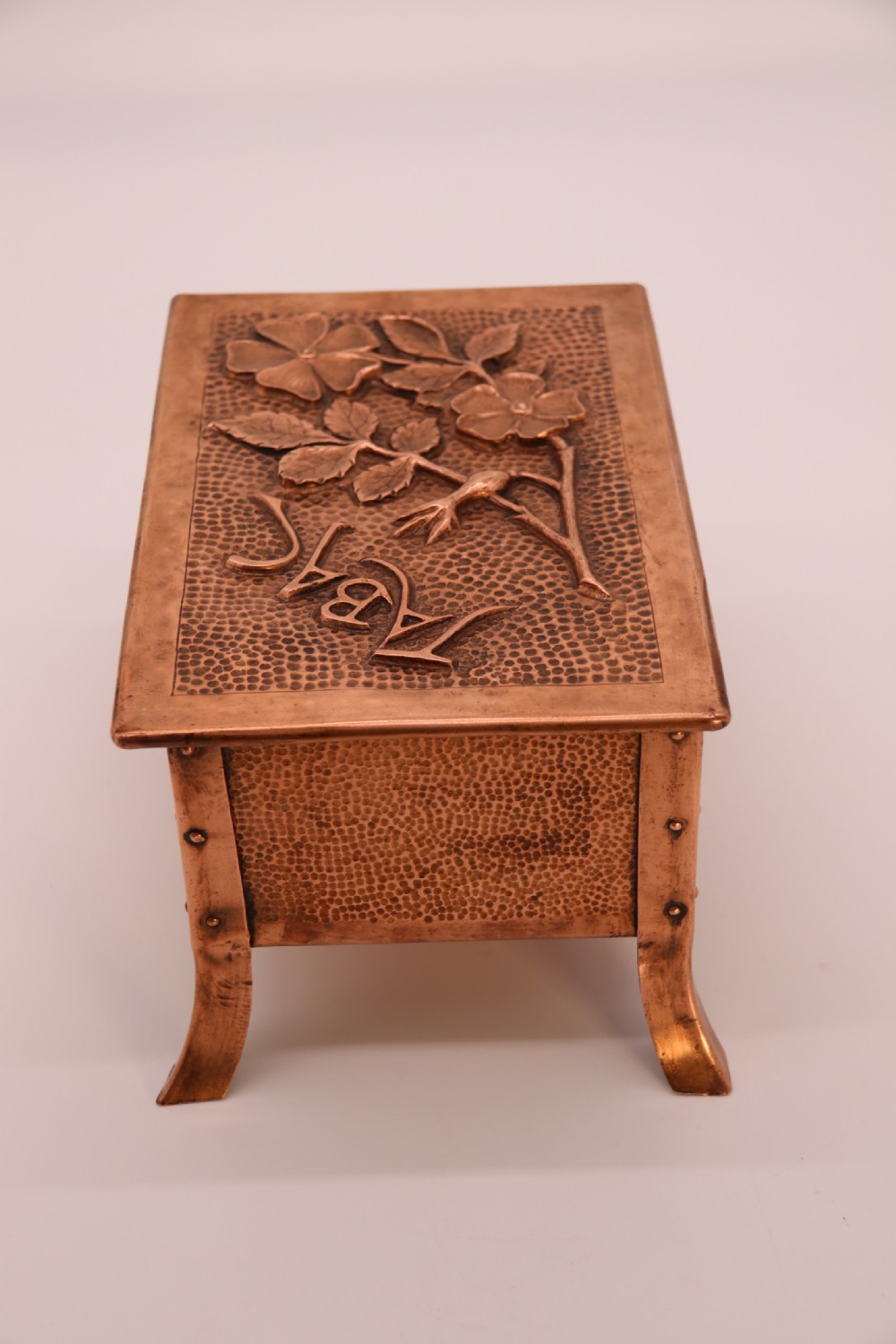 A rectangular Arts and Crafts copper box featuring a hand-hammered texture, splayed legs, and an embossed lid with a floral design and the word TABAC. View III