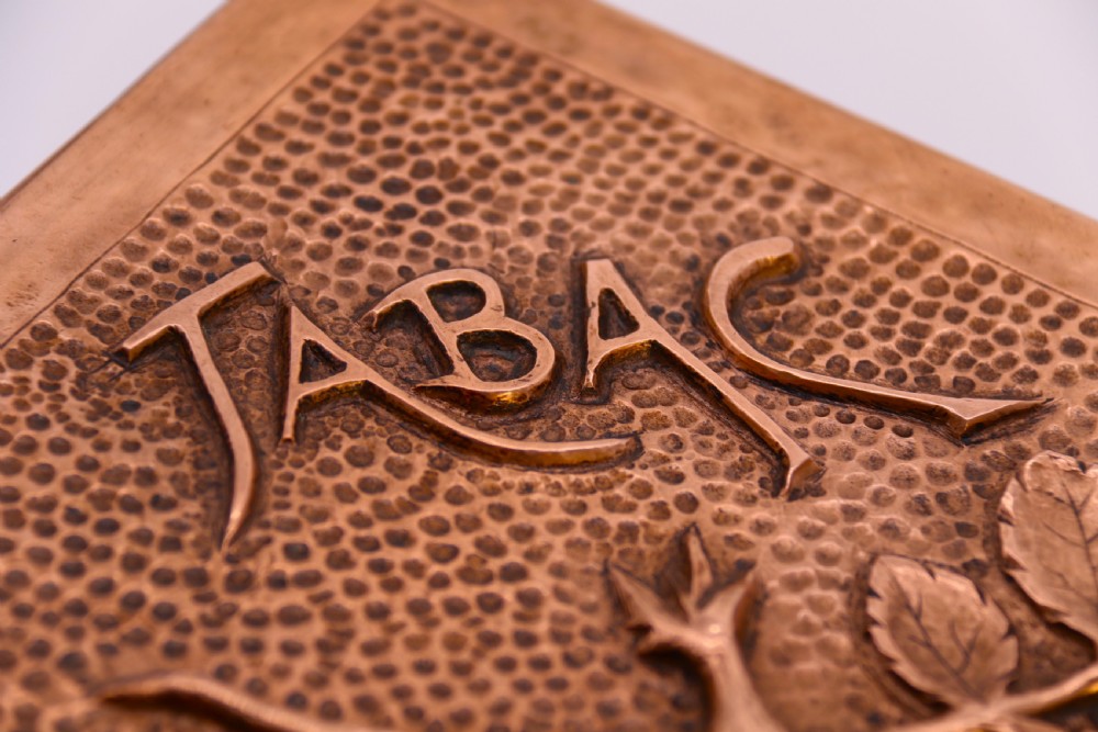 A rectangular Arts and Crafts copper box featuring a hand-hammered texture, splayed legs, and an embossed lid with a floral design and the word TABAC. View VII