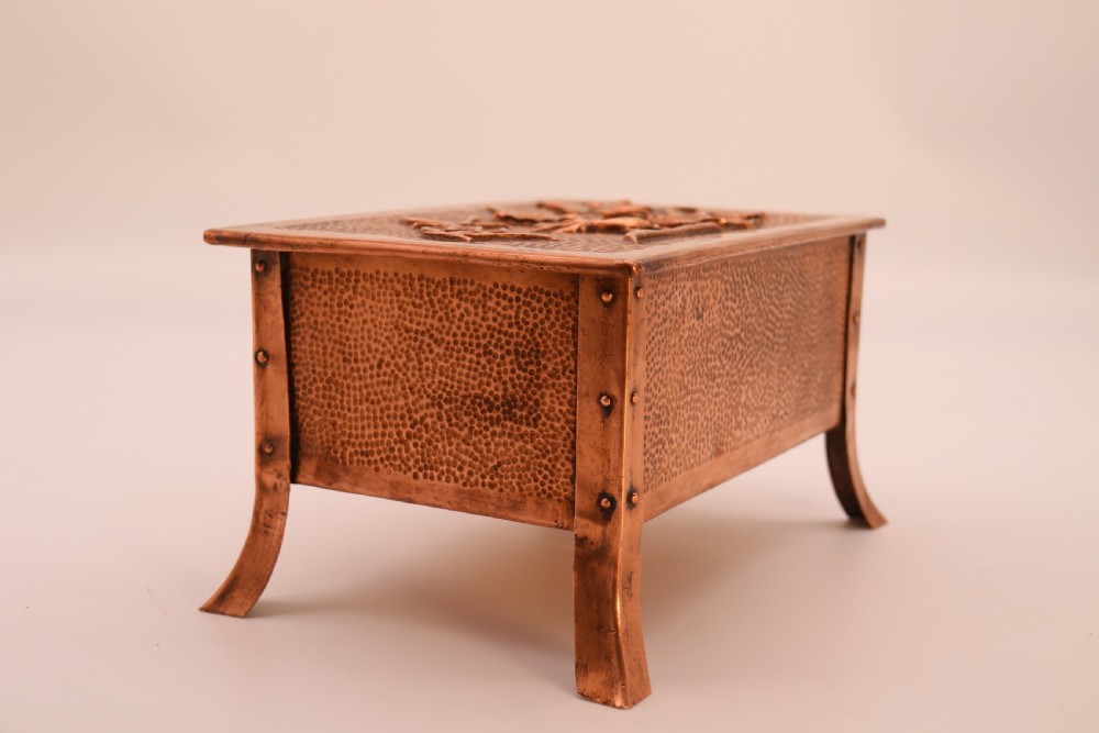 A rectangular Arts and Crafts copper box featuring a hand-hammered texture, splayed legs, and an embossed lid with a floral design and the word TABAC. View XII