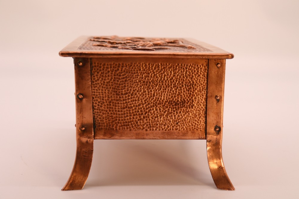 A rectangular Arts and Crafts copper box featuring a hand-hammered texture, splayed legs, and an embossed lid with a floral design and the word TABAC. View XIII