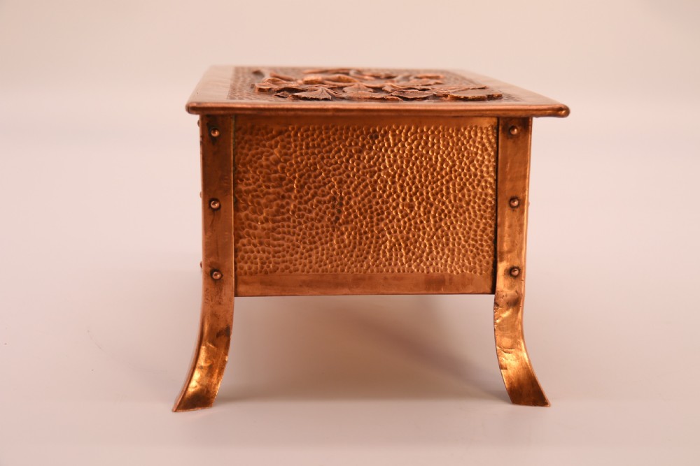 A rectangular Arts and Crafts copper box featuring a hand-hammered texture, splayed legs, and an embossed lid with a floral design and the word TABAC. View XIV