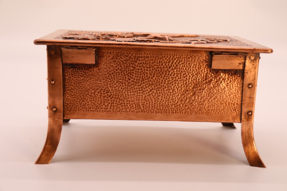 A rectangular Arts and Crafts copper box featuring a hand-hammered texture, splayed legs, and an embossed lid with a floral design and the word TABAC. View XVII