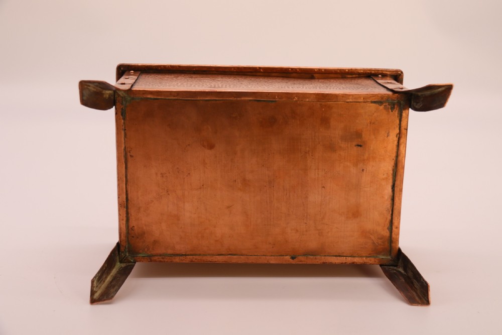 A rectangular Arts and Crafts copper box featuring a hand-hammered texture, splayed legs, and an embossed lid with a floral design and the word TABAC. View XVIII
